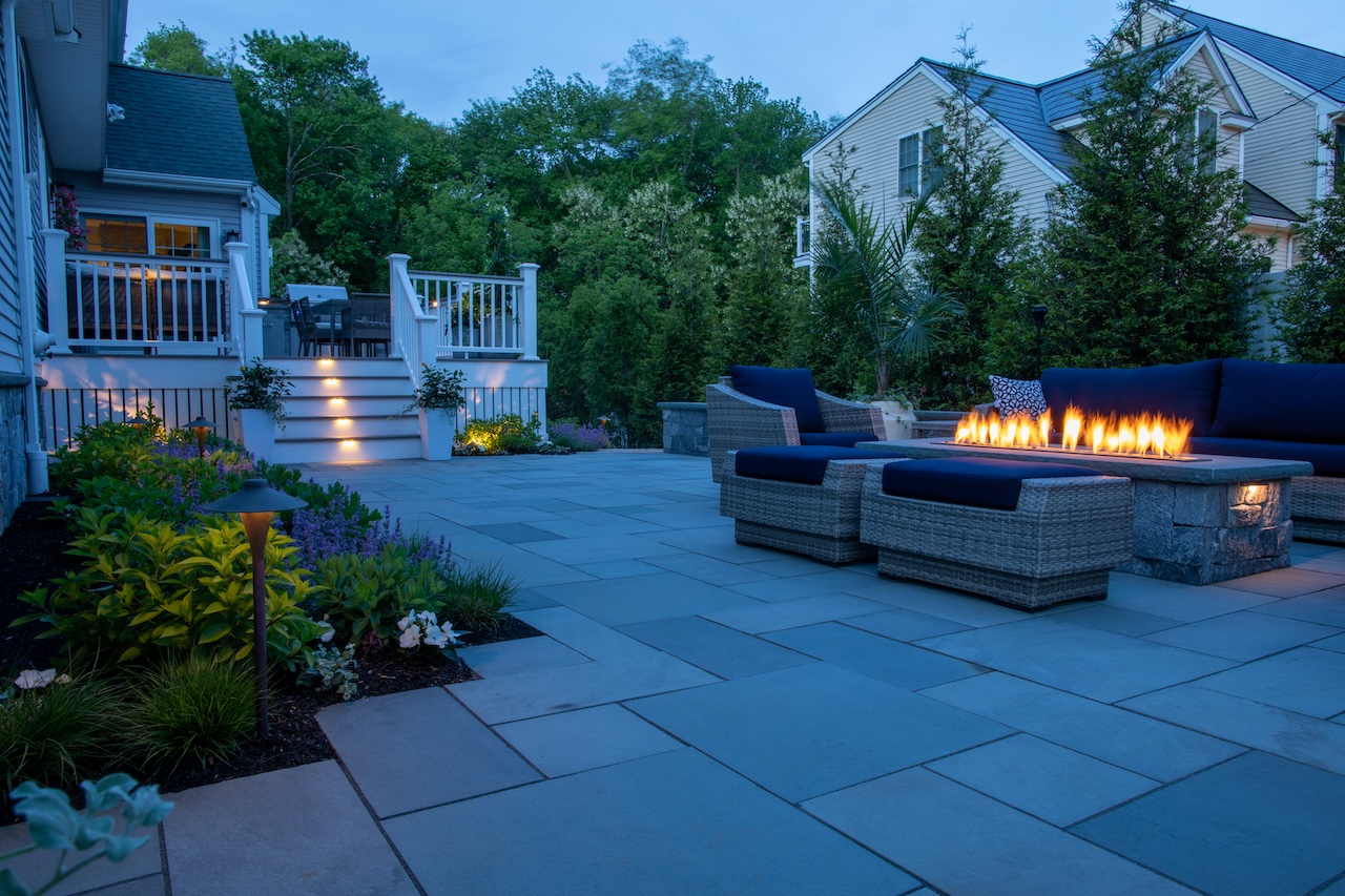 Explore the latest patio design trends including fire pits, seating walls, outdoor kitchens, and custom hardscape features that enhance outdoor living and property value.